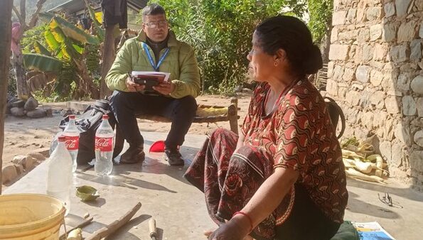 A Nepali man sits speaking to a woman outside her home in the mountains
