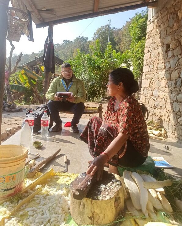 A Nepali man sits speaking to a woman outside her home in the mountains