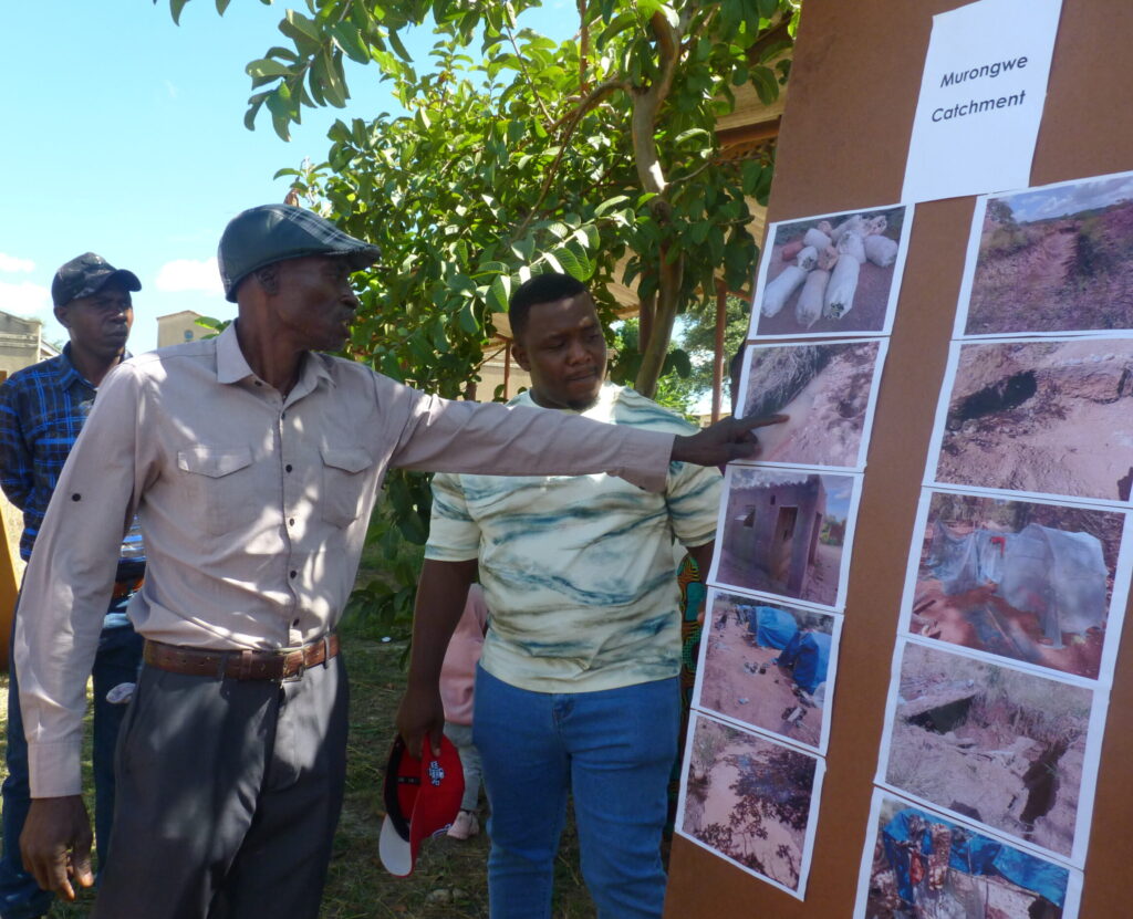 An older Zimbabwean man in a shirt and cap talks to a board of photos he took while others watch on